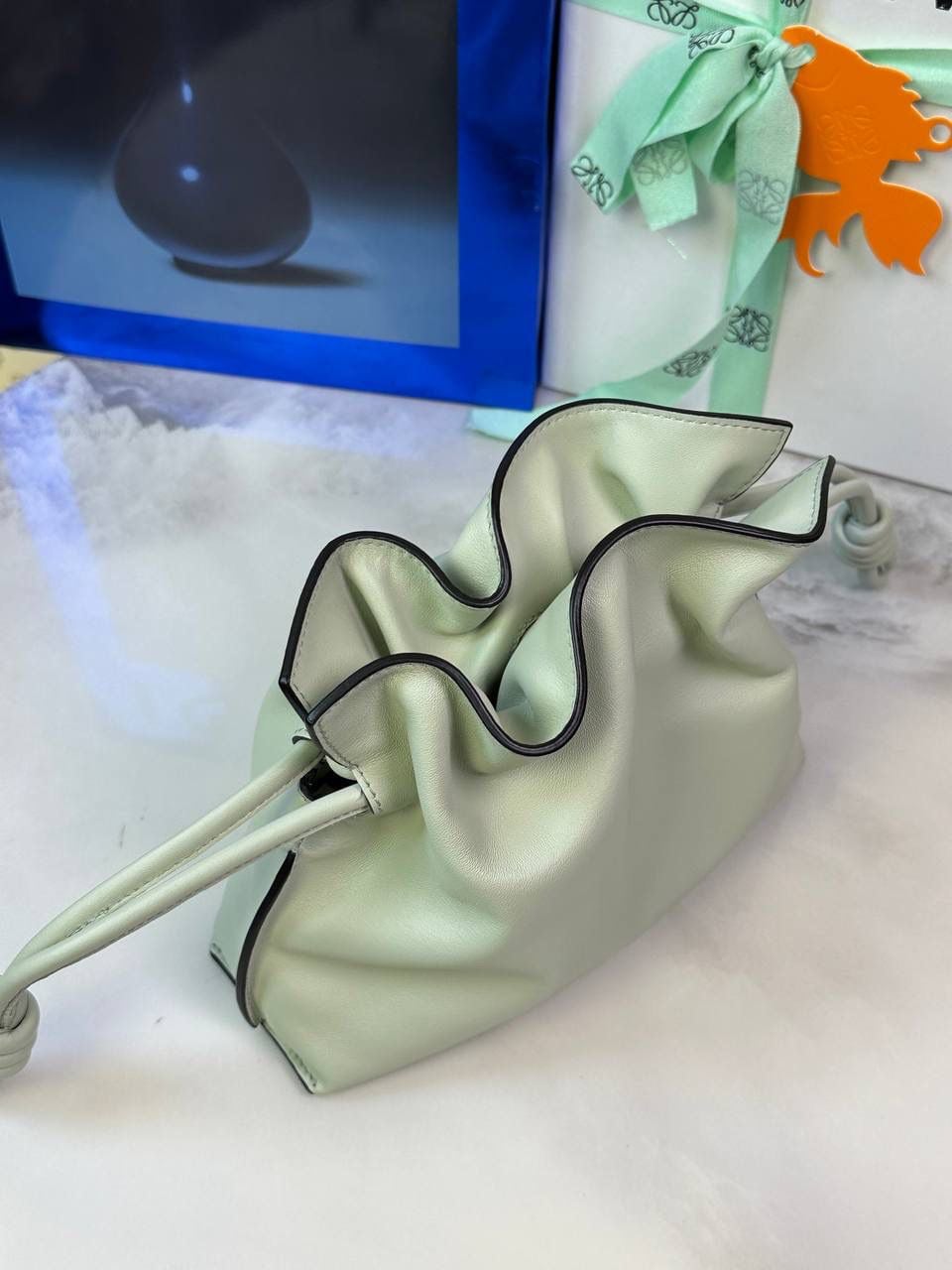 Flamenco clutch-NEW ✦迷你✦ 尺寸：𝟐𝟐.𝟓-𝟏𝟖-𝟗𝐜𝐦 型号：052030亮灰绿 ❤️mini flamenco clutch bag 可手拿亦可优雅斜挎 云朵般温暖亦轻盈的造型如此简单，💯耐看💯不会out的款式！ ❤️包袋采用进口小牛皮，手感如羊皮般细腻柔软，却比羊皮更加结实耐用，麂皮内衬 ❤️品牌标志性绳结设计，收紧袋口就是小福袋造型，超Q，看着不大实际超会装😇