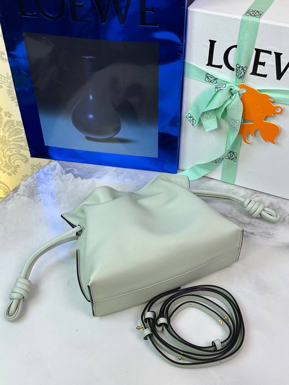 Flamenco clutch-NEW ✦迷你✦ 尺寸：𝟐𝟐.𝟓-𝟏𝟖-𝟗𝐜𝐦 型号：052030亮灰绿 ❤️mini flamenco clutch bag 可手拿亦可优雅斜挎 云朵般温暖亦轻盈的造型如此简单，💯耐看💯不会out的款式！ ❤️包袋采用进口小牛皮，手感如羊皮般细腻柔软，却比羊皮更加结实耐用，麂皮内衬 ❤️品牌标志性绳结设计，收紧袋口就是小福袋造型，超Q，看着不大实际超会装😇