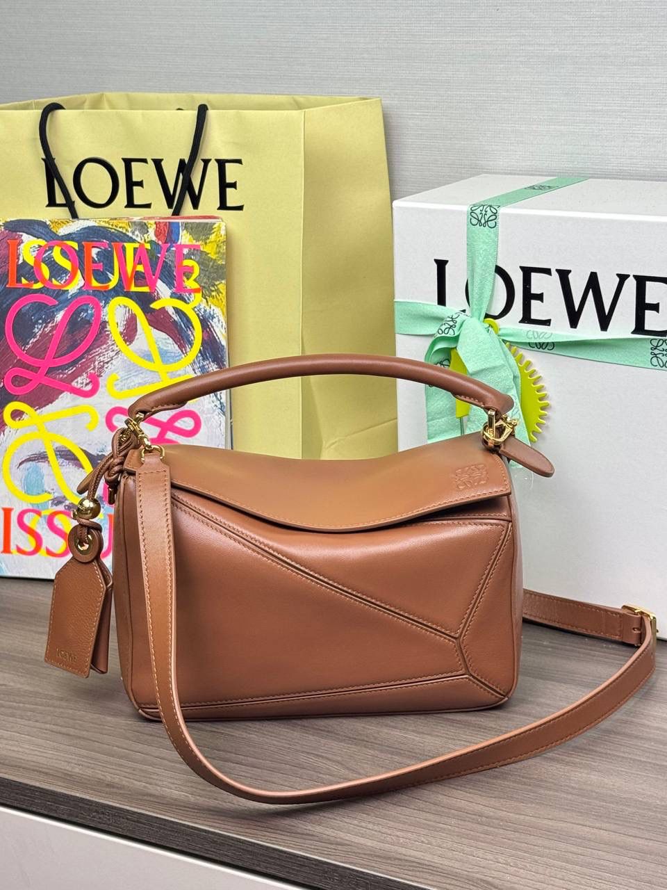 🎈【周年限定】 小号纳帕羊皮𝗙𝗲𝗮𝘁𝗵𝗲𝗿𝗹𝗶𝗴𝗵𝘁 𝗣𝘂𝘇𝘇𝗹𝗲手袋👜 ——山核桃色到货❤️ 尺寸：𝟮𝟰-𝟭𝟬.𝟱-𝟭𝟲.𝟱𝗰𝗺 编码：061610【配全套礼盒】 ✅延续经典老款𝗣𝘂𝘇𝘇𝗹𝗲做法，全新𝗣𝘂𝘇𝘇𝗹𝗲内外采用柔软轻盈的纳帕羊皮材质，为手袋注入随性慵懒的风格。 ✅该款饰有旋转卡扣，铰链式拉链头，一个外部拉链后袋，一个内部插袋，以及可拆卸式的𝗟𝗢𝗘𝗪𝗘烫金或烫银标签，饰有隐秘口袋和气球骰子，底部长方形金属脚钉。搭配可拆卸可调节长肩带，可肩背、斜挎或手提。