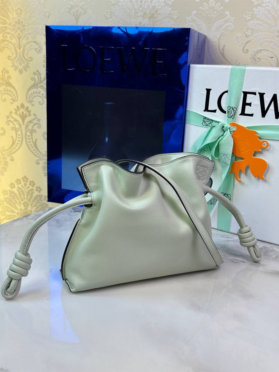 Flamenco clutch-NEW ✦迷你✦ 尺寸：𝟐𝟐.𝟓-𝟏𝟖-𝟗𝐜𝐦 型号：052030亮灰绿 ❤️mini flamenco clutch bag 可手拿亦可优雅斜挎 云朵般温暖亦轻盈的造型如此简单，💯耐看💯不会out的款式！ ❤️包袋采用进口小牛皮，手感如羊皮般细腻柔软，却比羊皮更加结实耐用，麂皮内衬 ❤️品牌标志性绳结设计，收紧袋口就是小福袋造型，超Q，看着不大实际超会装😇