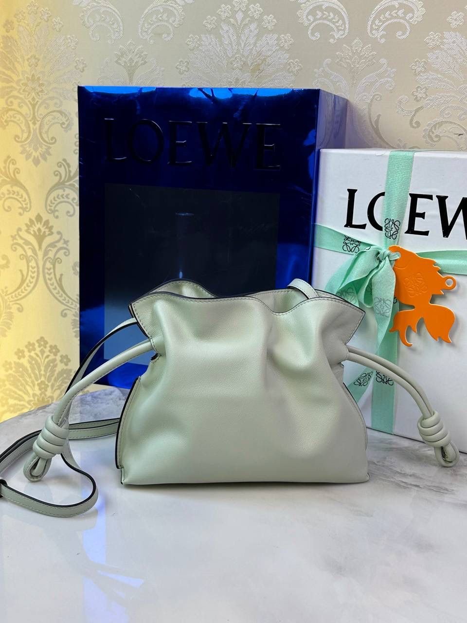 Flamenco clutch-NEW ✦迷你✦ 尺寸：𝟐𝟐.𝟓-𝟏𝟖-𝟗𝐜𝐦 型号：052030亮灰绿 ❤️mini flamenco clutch bag 可手拿亦可优雅斜挎 云朵般温暖亦轻盈的造型如此简单，💯耐看💯不会out的款式！ ❤️包袋采用进口小牛皮，手感如羊皮般细腻柔软，却比羊皮更加结实耐用，麂皮内衬 ❤️品牌标志性绳结设计，收紧袋口就是小福袋造型，超Q，看着不大实际超会装😇