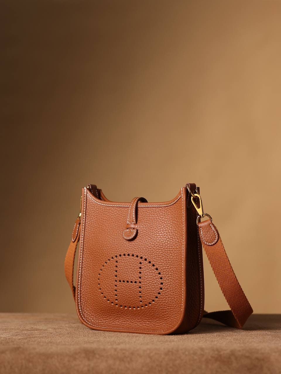 HERMES爱马仕Evelyne 16伊芙琳金棕金扣👜✨ TaurillonMaurice 小公牛皮 尺寸：16*18*5cm 爱马仕Evelyne伊芙琳 Evelyne包的设计灵感来自于一种名为“马鞍袋”的马具袋，这是一种常用于骑手和马车夫的袋子，用于储存和运输马具和其他必需品。 爱马仕将这种马具袋的经典元素与品牌的手工艺传统相结合，打造出了具有时尚感和功能性的包包。 因此，伊芙琳包不仅是一款实用的手提包，同时也代表着品牌深厚的历史和文化传统❤️