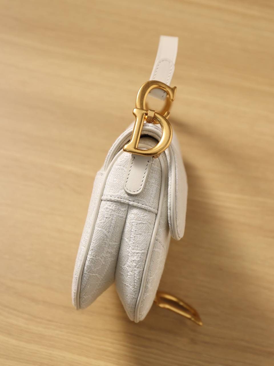 马鞍包白色小号 独家渠道原厂货 尺寸：21 x 18 x 5 厘米 这款标志性的马鞍包由玛丽亚·嘉茜娅·蔻丽 (Maria Grazia Chiuri) 设计，重新演绎经典款式。 马镫“D”形吊饰和马鞍翻盖彰显品牌经典设计，搭配磁铁搭扣，手柄两端饰以“CD”标志。 采用白色提花 Oblique 印花面料制作，饰以复古金色饰面金属配件。 这款马鞍包可手提或肩背，可搭配不同的肩带彰显个性。 马镫“D”形吊饰和磁铁搭扣开合 手柄饰以“CD”标志 内部口袋 后侧口袋 内含防尘袋