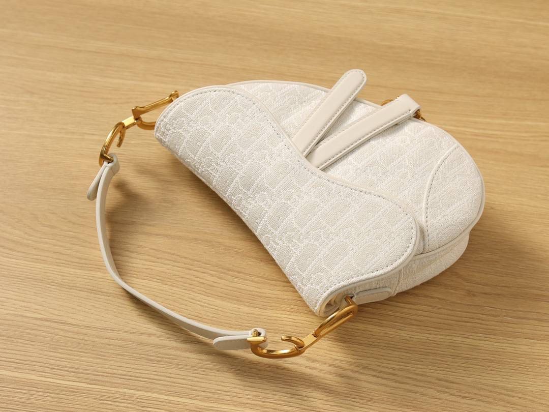 马鞍包白色小号 独家渠道原厂货 尺寸：21 x 18 x 5 厘米 这款标志性的马鞍包由玛丽亚·嘉茜娅·蔻丽 (Maria Grazia Chiuri) 设计，重新演绎经典款式。 马镫“D”形吊饰和马鞍翻盖彰显品牌经典设计，搭配磁铁搭扣，手柄两端饰以“CD”标志。 采用白色提花 Oblique 印花面料制作，饰以复古金色饰面金属配件。 这款马鞍包可手提或肩背，可搭配不同的肩带彰显个性。 马镫“D”形吊饰和磁铁搭扣开合 手柄饰以“CD”标志 内部口袋 后侧口袋 内含防尘袋