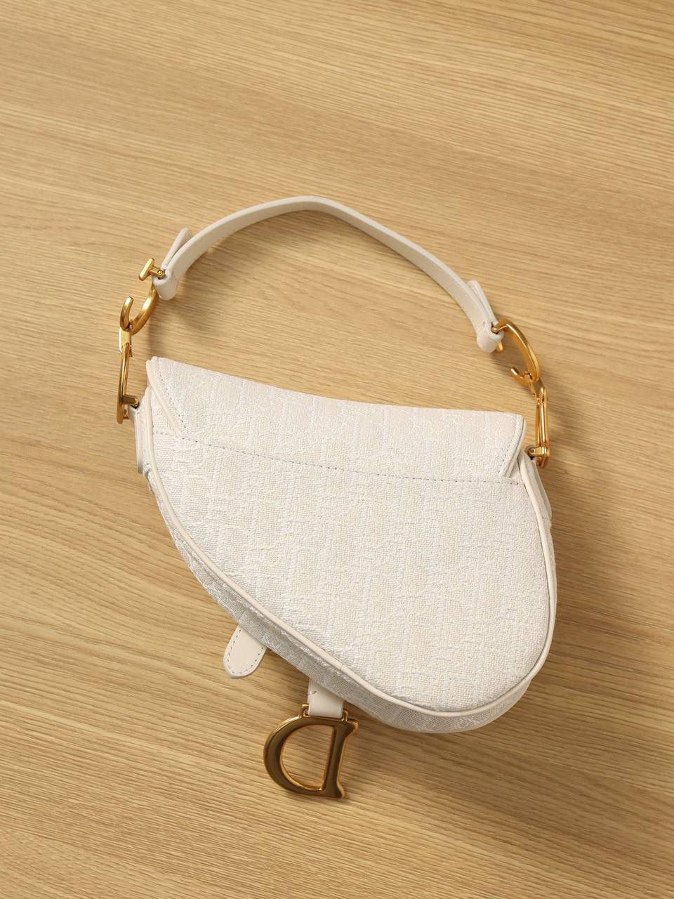 马鞍包白色小号 独家渠道原厂货 尺寸：21 x 18 x 5 厘米 这款标志性的马鞍包由玛丽亚·嘉茜娅·蔻丽 (Maria Grazia Chiuri) 设计，重新演绎经典款式。 马镫“D”形吊饰和马鞍翻盖彰显品牌经典设计，搭配磁铁搭扣，手柄两端饰以“CD”标志。 采用白色提花 Oblique 印花面料制作，饰以复古金色饰面金属配件。 这款马鞍包可手提或肩背，可搭配不同的肩带彰显个性。 马镫“D”形吊饰和磁铁搭扣开合 手柄饰以“CD”标志 内部口袋 后侧口袋 内含防尘袋