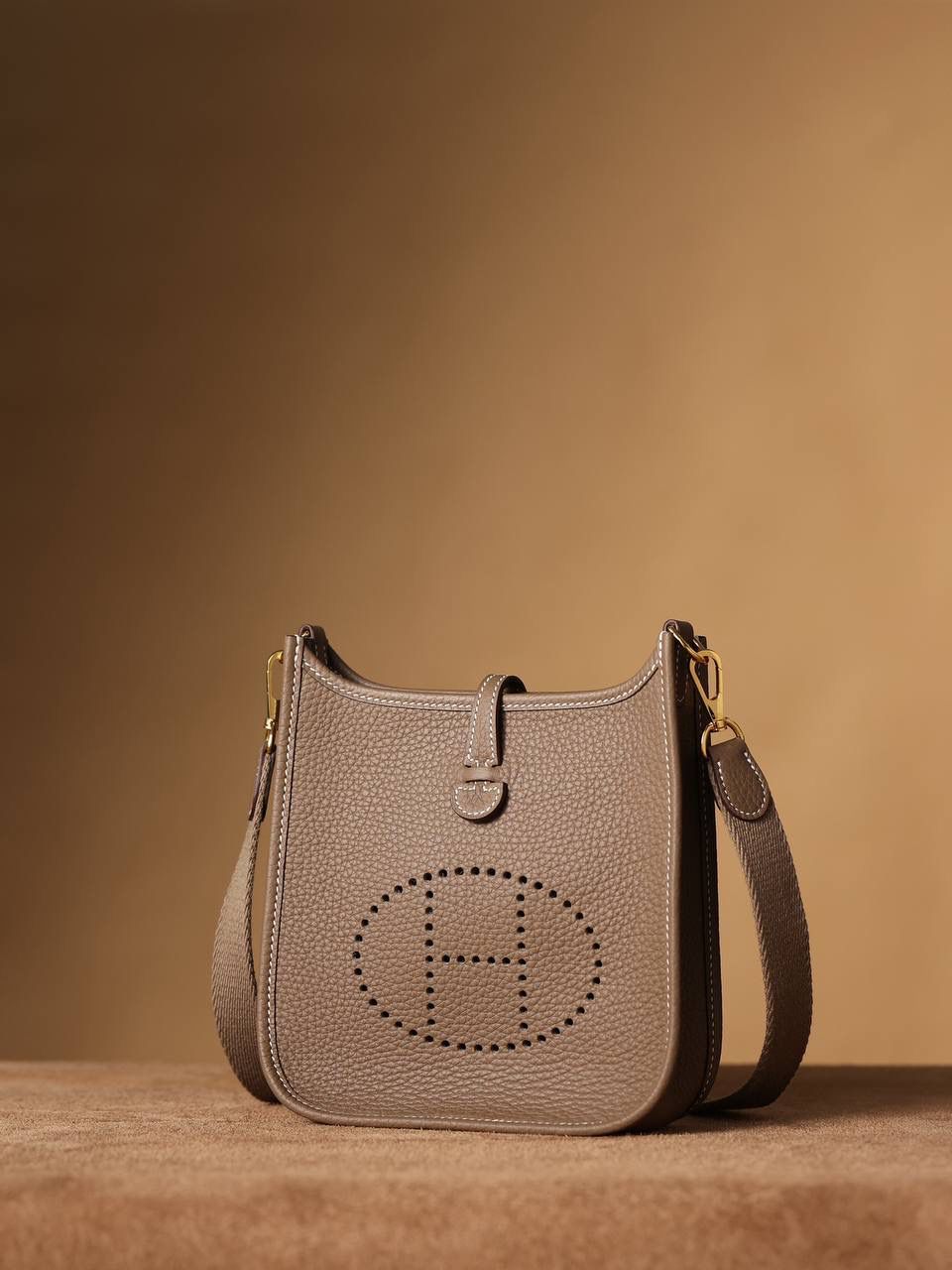 HERMES爱马仕Evelyne 16伊芙琳大象灰金扣👜✨ TaurillonMaurice 小公牛皮 尺寸：16*18*5cm 爱马仕Evelyne伊芙琳 Evelyne包的设计灵感来自于一种名为“马鞍袋”的马具袋，这是一种常用于骑手和马车夫的袋子，用于储存和运输马具和其他必需品。 爱马仕将这种马具袋的经典元素与品牌的手工艺传统相结合，打造出了具有时尚感和功能性的包包。 因此，伊芙琳包不仅是一款实用的手提包，同时也代表着品牌深厚的历史和文化传统❤️