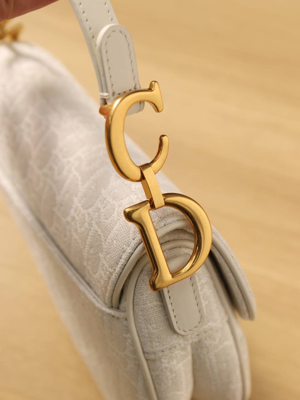 马鞍包白色小号 独家渠道原厂货 尺寸：21 x 18 x 5 厘米 这款标志性的马鞍包由玛丽亚·嘉茜娅·蔻丽 (Maria Grazia Chiuri) 设计，重新演绎经典款式。 马镫“D”形吊饰和马鞍翻盖彰显品牌经典设计，搭配磁铁搭扣，手柄两端饰以“CD”标志。 采用白色提花 Oblique 印花面料制作，饰以复古金色饰面金属配件。 这款马鞍包可手提或肩背，可搭配不同的肩带彰显个性。 马镫“D”形吊饰和磁铁搭扣开合 手柄饰以“CD”标志 内部口袋 后侧口袋 内含防尘袋