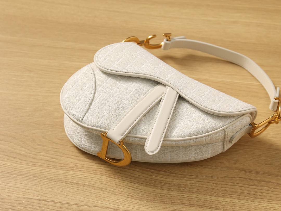 马鞍包白色小号 独家渠道原厂货 尺寸：21 x 18 x 5 厘米 这款标志性的马鞍包由玛丽亚·嘉茜娅·蔻丽 (Maria Grazia Chiuri) 设计，重新演绎经典款式。 马镫“D”形吊饰和马鞍翻盖彰显品牌经典设计，搭配磁铁搭扣，手柄两端饰以“CD”标志。 采用白色提花 Oblique 印花面料制作，饰以复古金色饰面金属配件。 这款马鞍包可手提或肩背，可搭配不同的肩带彰显个性。 马镫“D”形吊饰和磁铁搭扣开合 手柄饰以“CD”标志 内部口袋 后侧口袋 内含防尘袋