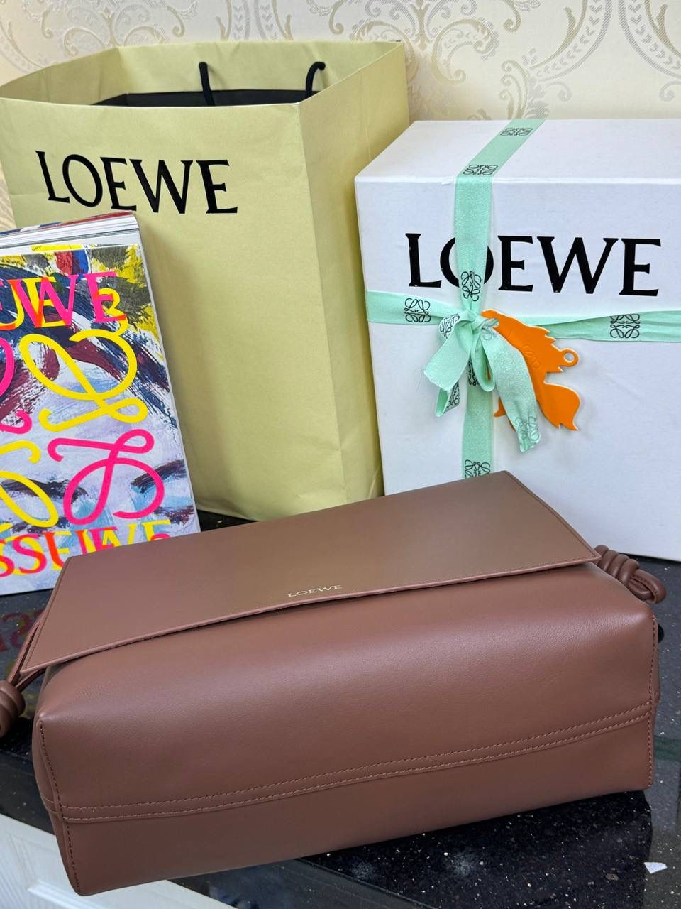 【全皮布朗尼色】 𝙇𝙤𝙚𝙬𝙚 𝙁𝙡𝙖𝙢𝙚𝙣𝙘𝙤 𝙎𝙖𝙩𝙘𝙝𝙚𝙡 福袋款邮差包 ➕刺绣🅾️字母宽肩带 编码：062404 尺寸：𝟑𝟒-𝟏𝟐-𝟐𝟒𝐜𝐦 新款以经典福袋收缩打结为元素，采用内部麂皮➕外部进口小牛皮➕刺绣字母宽肩带的精致搭配打造全新升级款邮差包🅰️，可斜挎、肩背和手提，超大容量满足日常所需🎈