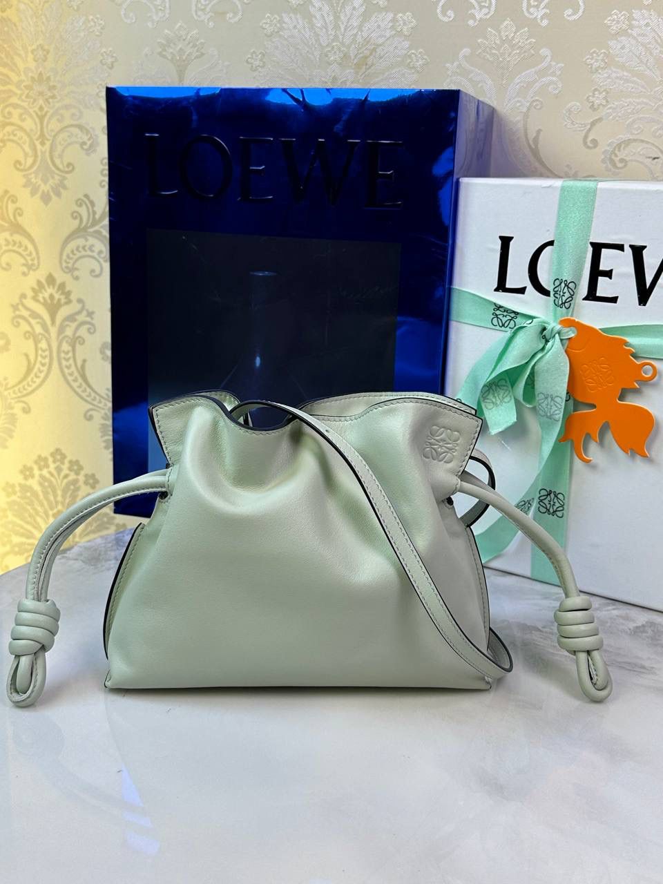 Flamenco clutch-NEW ✦迷你✦ 尺寸：𝟐𝟐.𝟓-𝟏𝟖-𝟗𝐜𝐦 型号：052030亮灰绿 ❤️mini flamenco clutch bag 可手拿亦可优雅斜挎 云朵般温暖亦轻盈的造型如此简单，💯耐看💯不会out的款式！ ❤️包袋采用进口小牛皮，手感如羊皮般细腻柔软，却比羊皮更加结实耐用，麂皮内衬 ❤️品牌标志性绳结设计，收紧袋口就是小福袋造型，超Q，看着不大实际超会装😇