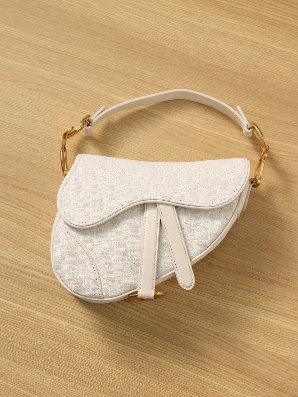 马鞍包白色小号 独家渠道原厂货 尺寸：21 x 18 x 5 厘米 这款标志性的马鞍包由玛丽亚·嘉茜娅·蔻丽 (Maria Grazia Chiuri) 设计，重新演绎经典款式。 马镫“D”形吊饰和马鞍翻盖彰显品牌经典设计，搭配磁铁搭扣，手柄两端饰以“CD”标志。 采用白色提花 Oblique 印花面料制作，饰以复古金色饰面金属配件。 这款马鞍包可手提或肩背，可搭配不同的肩带彰显个性。 马镫“D”形吊饰和磁铁搭扣开合 手柄饰以“CD”标志 内部口袋 后侧口袋 内含防尘袋