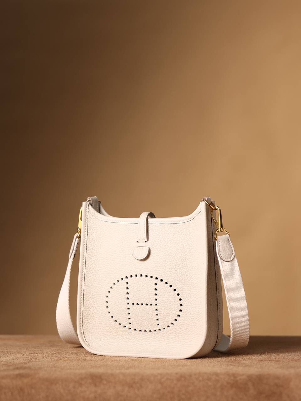 HERMES爱马仕Evelyne 16伊芙琳奶昔白金扣👜✨ TaurillonMaurice 小公牛皮 尺寸：16*18*5cm 爱马仕Evelyne伊芙琳 Evelyne包的设计灵感来自于一种名为“马鞍袋”的马具袋，这是一种常用于骑手和马车夫的袋子，用于储存和运输马具和其他必需品。 爱马仕将这种马具袋的经典元素与品牌的手工艺传统相结合，打造出了具有时尚感和功能性的包包。 因此，伊芙琳包不仅是一款实用的手提包，同时也代表着品牌深厚的历史和文化传统❤️